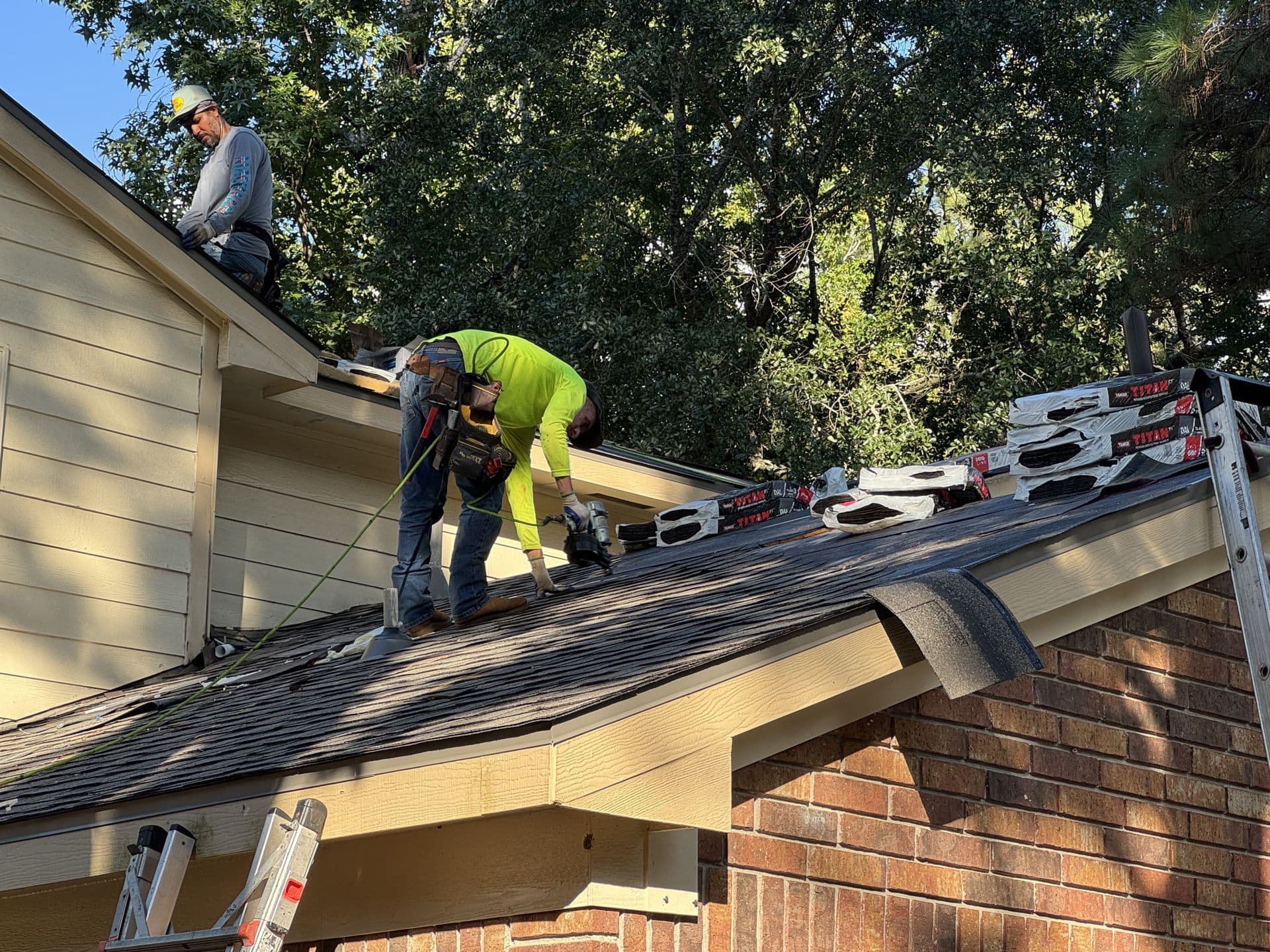True Line crew repairing shingles at the edge of a brick home's roof